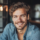 Homme souriant avec cheveux bouclés et chemise bleue.